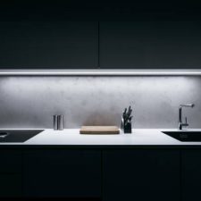 Modern kitchen in minimalist design during night with LED light strip and premium materials such as glass and concrete.Kitchen is complemented by basic kitchen utensils made of high quality materials.